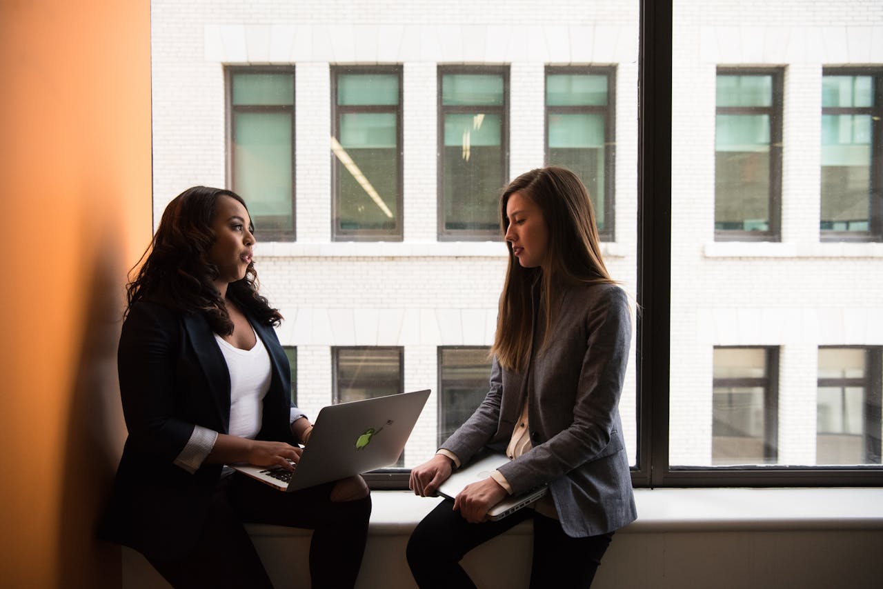 Two women having a business discussion in an office setting, using a laptop.