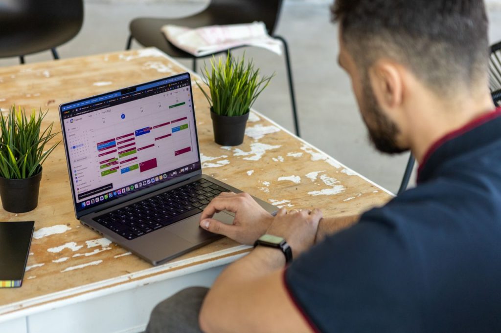 pexels photo 11836060 11836060 Man working remotely at a desk with a laptop open to a calendar app.