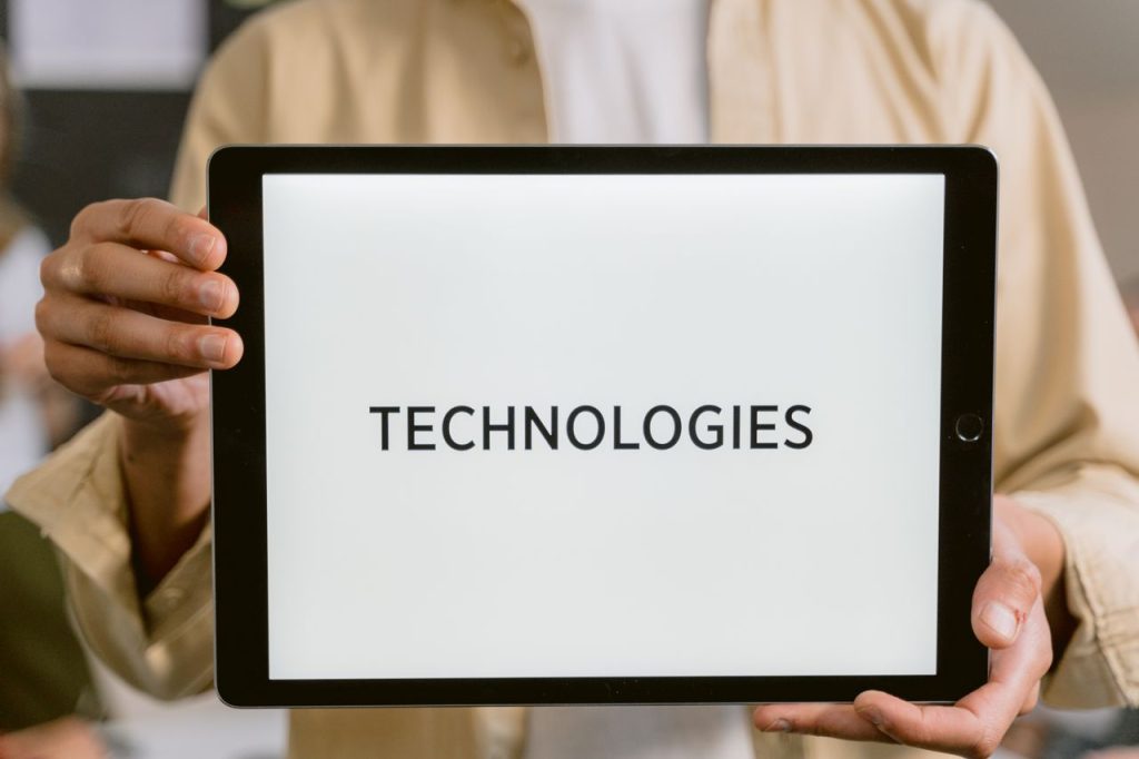 pexels photo 6913311 6913311 Close-up of a person holding a tablet with the word 'Technologies' on the screen.
